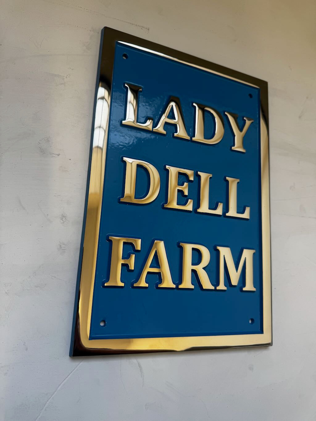 Blue sign with gold text 'LADY DELL FARM' on a white wall