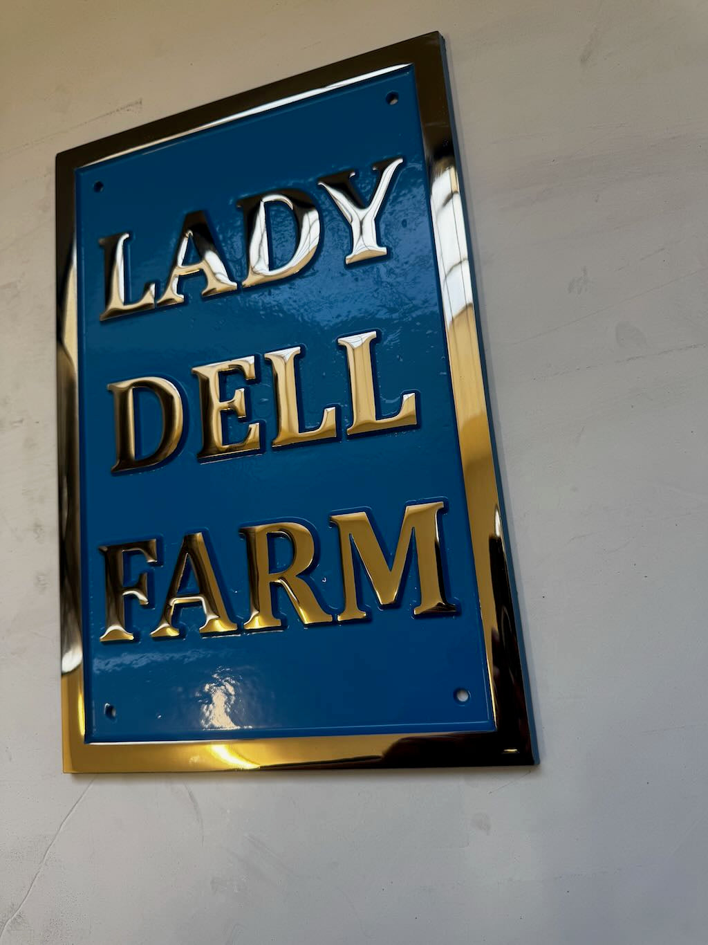 Blue sign with gold text 'LADY DELL FARM' on a white wall