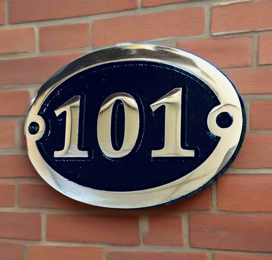 Oval black and silver house number 101 plaque on a brick wall.