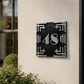 A modern black and silver house number plaque mounted on a textured beige stucco wall next to a dark door frame.