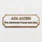 ADA Access sign with gold lettering and border on a white plaque, mounted on a textured off-white wall. The sign reads 'ADA ACCESS' and 'FOR ASSISTANCE PLEASE RING BELL'.