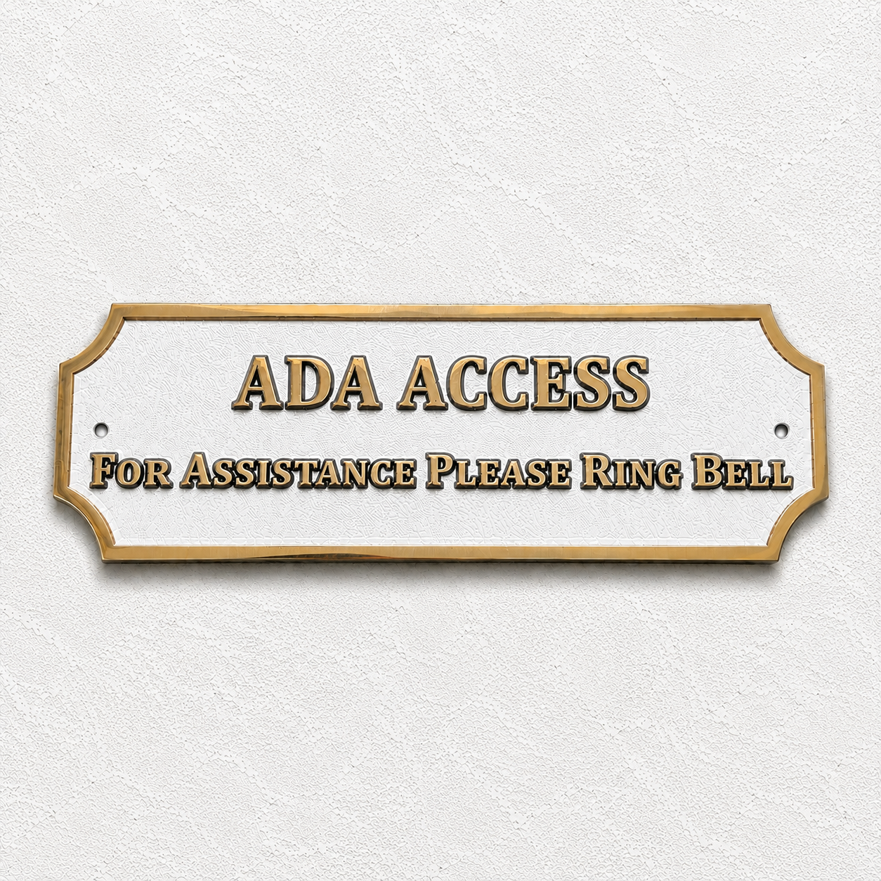ADA Access sign with gold lettering and border on a white plaque, mounted on a textured off-white wall. The sign reads 'ADA ACCESS' and 'FOR ASSISTANCE PLEASE RING BELL'.
