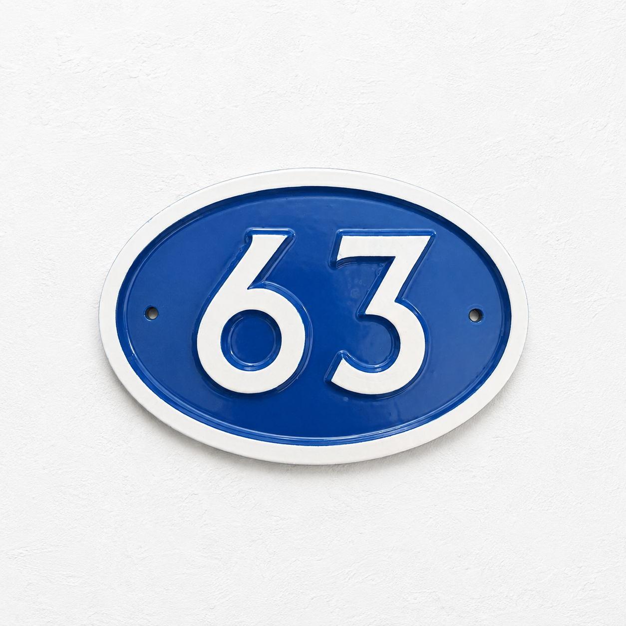 An oval blue and white house number plaque displaying '63' in raised white numerals, mounted on a textured white wall.