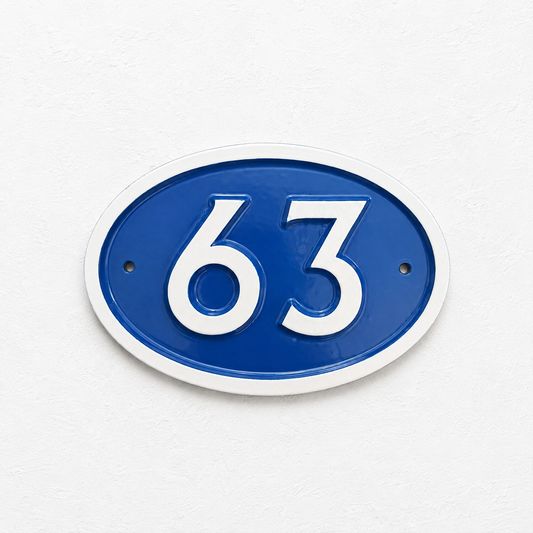 An oval blue and white house number plaque displaying '63' in raised white numerals, mounted on a textured white wall.