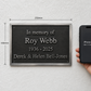 A memorial wall plaque with engraved silver text on a dark plaque, shown mounted on a white textured wall next to a hand holding an iPhone 14 to indicate scale. The image includes dimension lines showing the plaque's size as 250mm by 166mm.