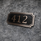 Cast bronze rectangle house number sign with raised numbers and double border mounted on exterior wall