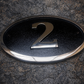 Cast bronze oval house number sign with polished raised numeral and black background
