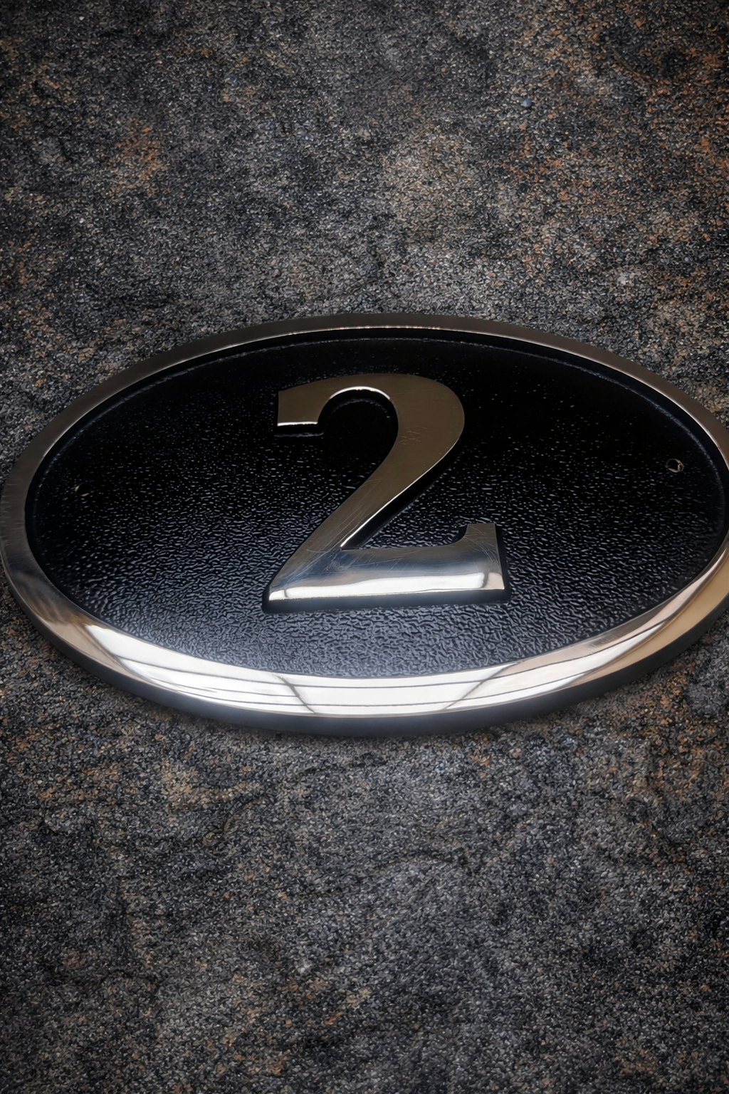 Cast bronze oval house number sign with polished raised numeral and black background
