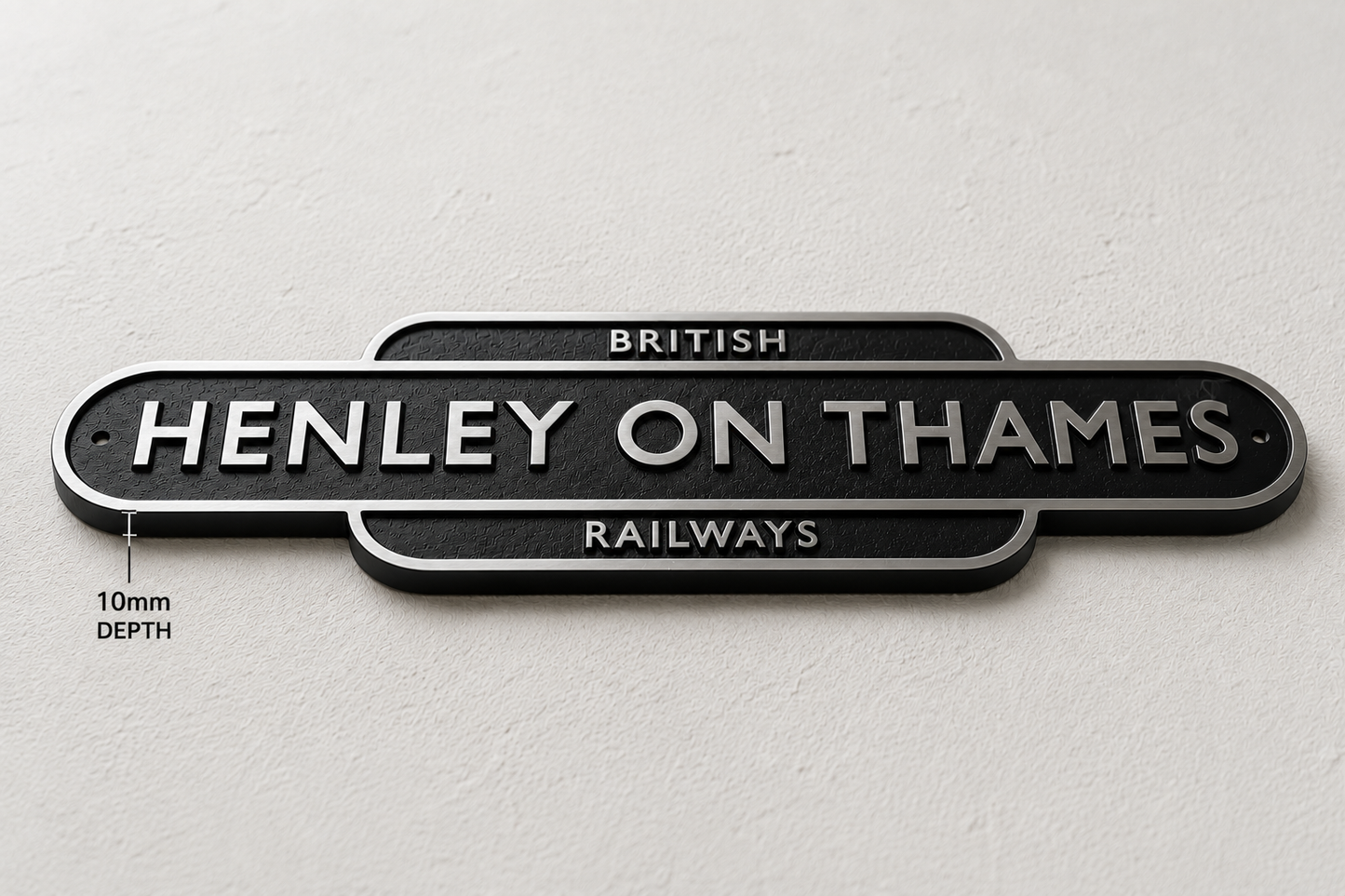 A black metal sign reading 'HENLEY ON THAMES RAILWAYS' with silver lettering, mounted on a light textured wall. Small text on the left indicates 10mm depth.