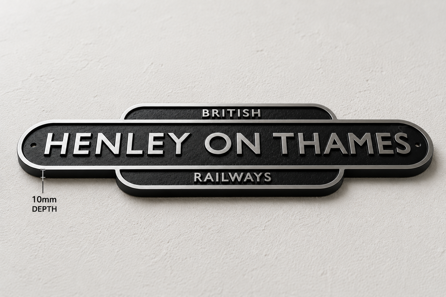 A black metal sign reading 'HENLEY ON THAMES RAILWAYS' with silver lettering, mounted on a light textured wall. Small text on the left indicates 10mm depth.