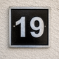 Cast aluminium square house number sign with raised brushed numerals black background and background fixing holes