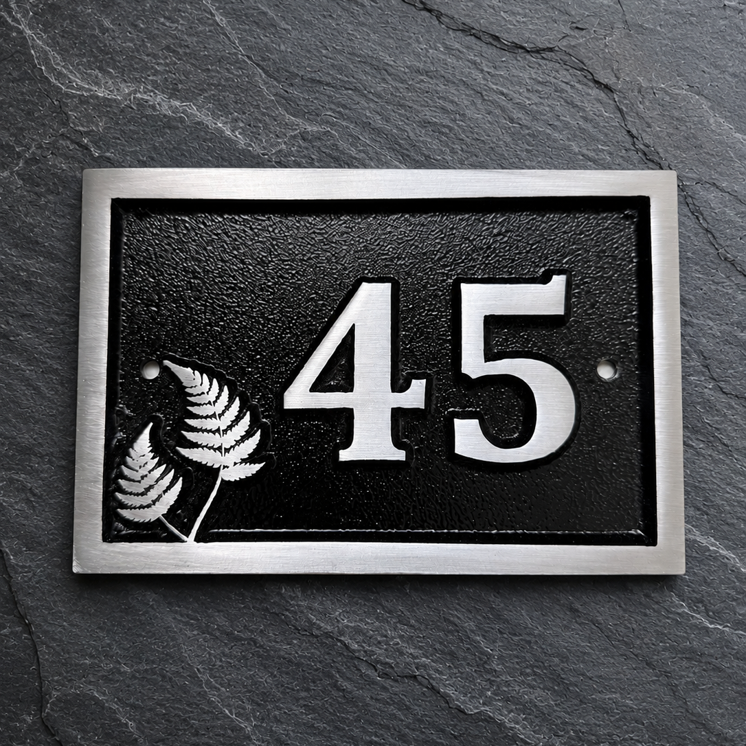 Personalised cast aluminium house number plaque featuring satin-finished number 45 with decorative fern motif and black textured background.