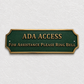 A rectangular ADA Access sign with a dark green background and gold lettering, mounted on a textured off-white wall. The sign reads 'ADA ACCESS' and 'FOR ASSISTANCE PLEASE RING BELL'.