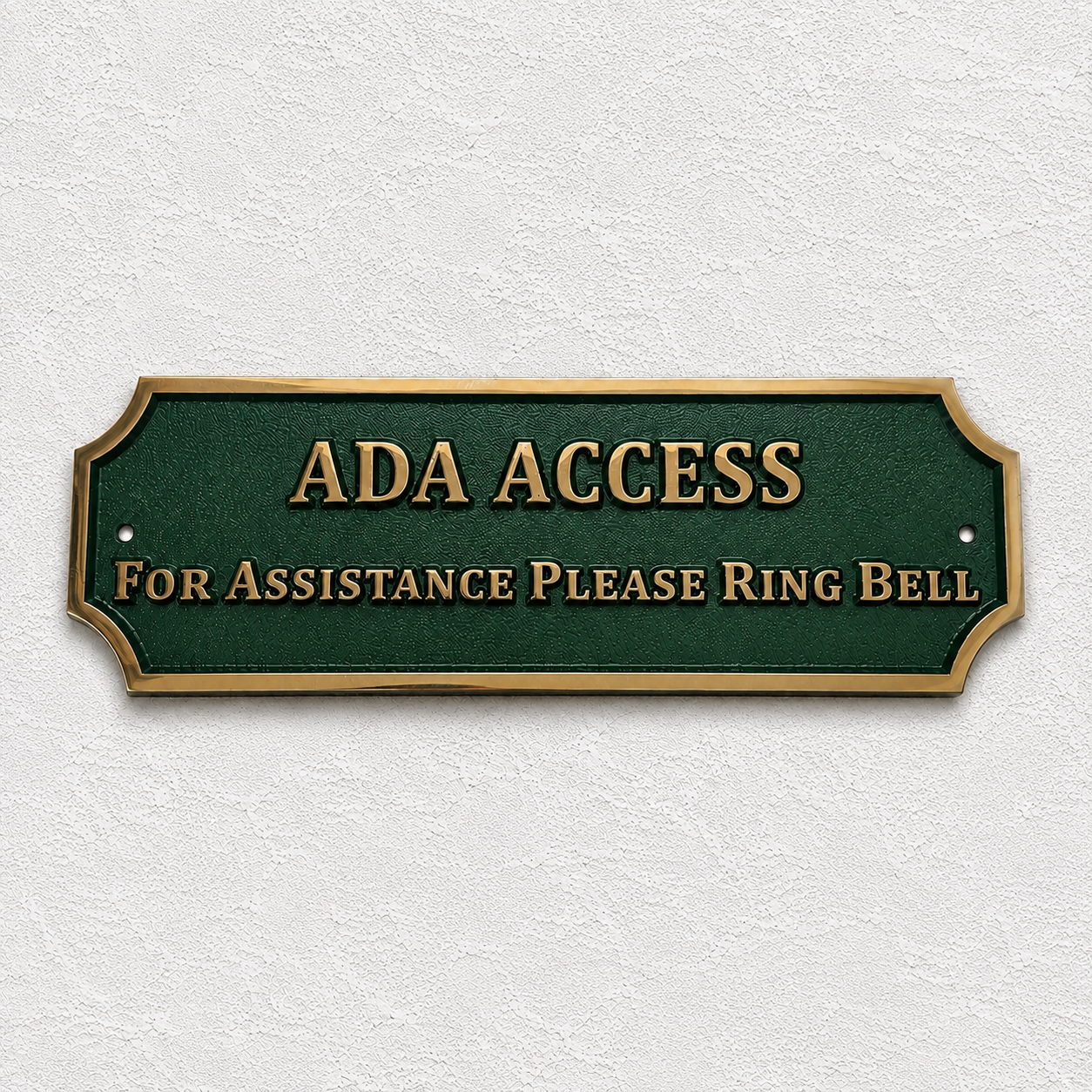 A rectangular ADA Access sign with a dark green background and gold lettering, mounted on a textured off-white wall. The sign reads 'ADA ACCESS' and 'FOR ASSISTANCE PLEASE RING BELL'.