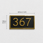A rectangular house number plaque with the numbers 367 in gold on a black background, shown on a light textured wall with dimension lines indicating 140mm height and 287mm width.