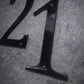 Black metal number '21' on a textured gray surface