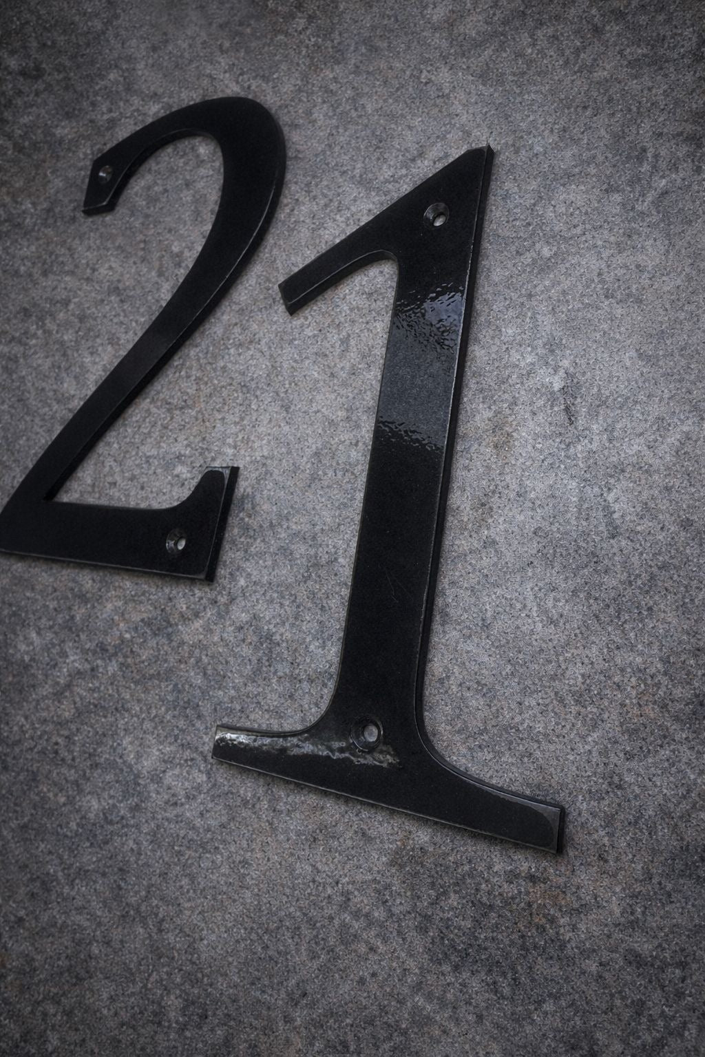 Black metal number '21' on a textured gray surface
