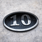Cast aluminium oval hotel room number sign with raised numbers and black background mounted on wall
