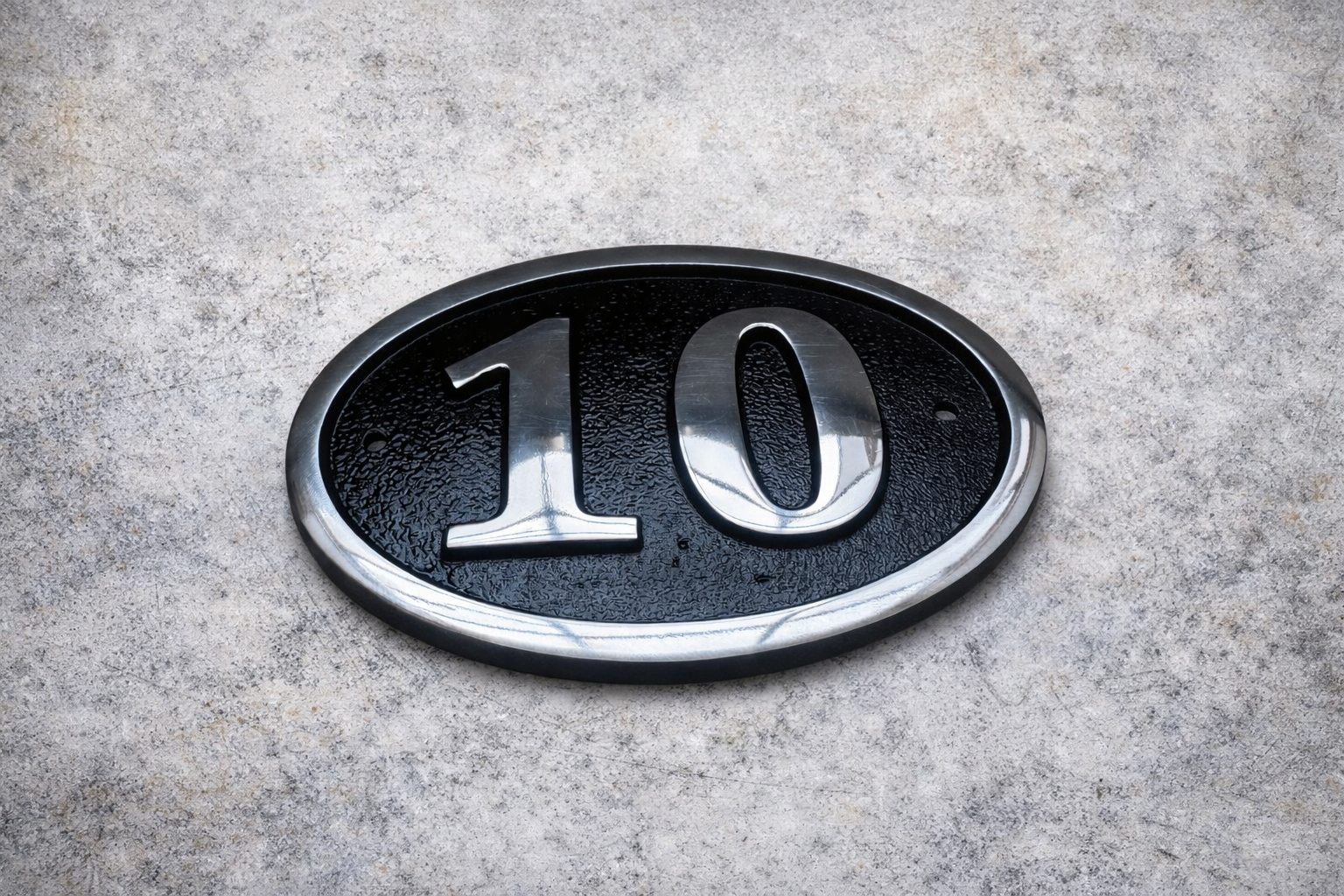 Cast aluminium oval hotel room number sign with raised numbers and black background mounted on wall