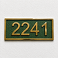 A rectangular house number plaque with raised gold numerals '2241' on a textured dark green background, mounted on a white textured wall.