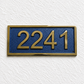 A rectangular house number plaque with raised gold numerals '2241' on a textured dark blue background, mounted on a white textured wall.