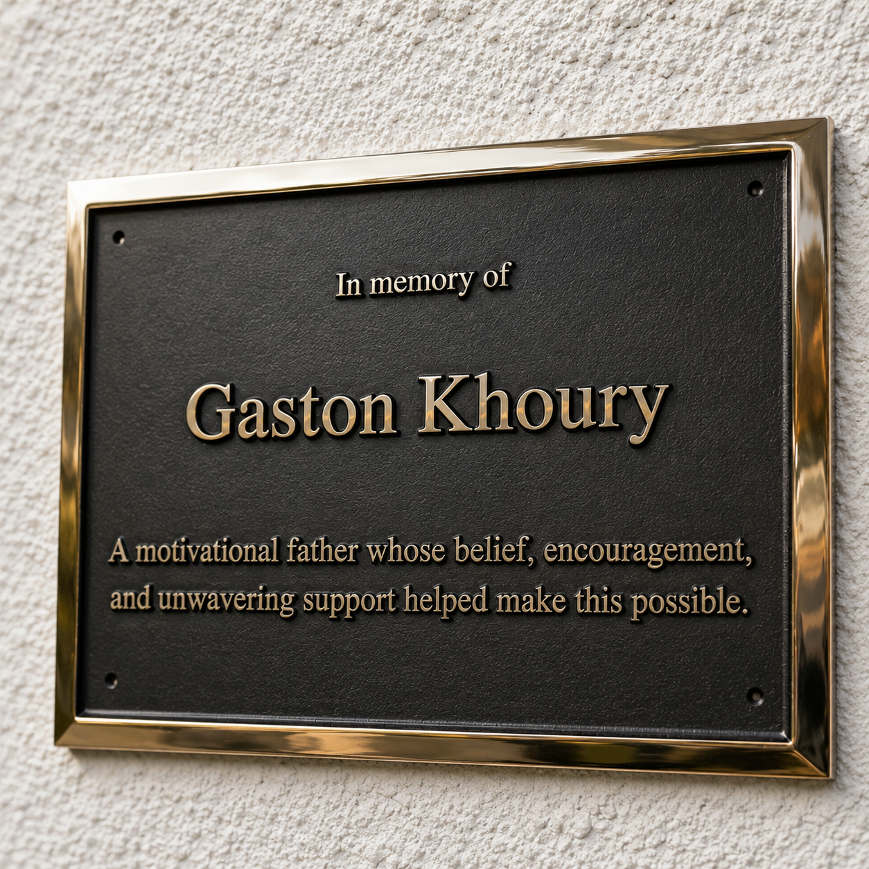 A rectangular black memorial plaque with a polished gold-toned metal border, mounted on a textured off-white wall. The plaque features raised gold lettering that reads 'In memory of Gaston Khoury' and a shorter descriptive quote below.