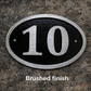 Cast aluminium oval hotel room number sign with raised numbers and black background mounted on wall