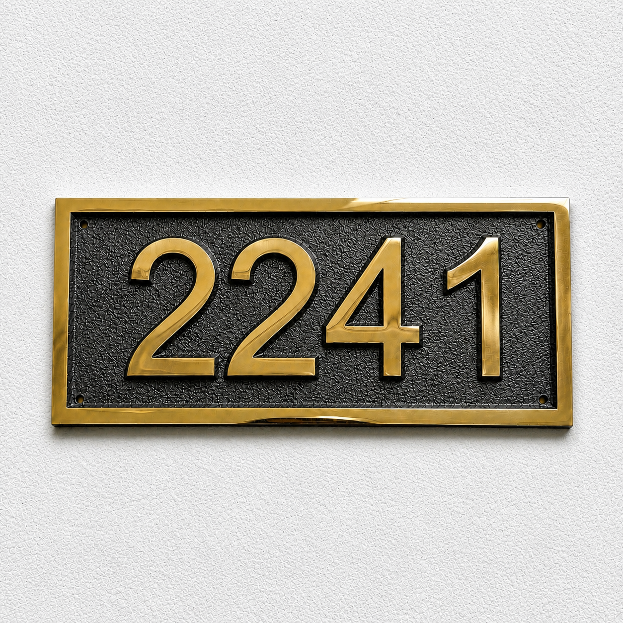 A rectangular house number plaque featuring the gold numerals '2241' on a textured black background, bordered by a polished gold frame, mounted on a light gray textured wall.
