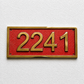 A rectangular house number plaque with the gold numerals '2241' on a textured red background, mounted on a white textured wall.