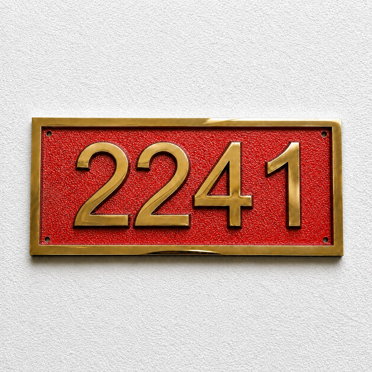 A rectangular house number plaque with the gold numerals '2241' on a textured red background, mounted on a white textured wall.