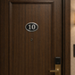 Cast aluminium oval hotel room number sign with raised numbers and black background mounted on wall