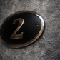 Cast bronze oval house number sign with polished raised numeral and black background
