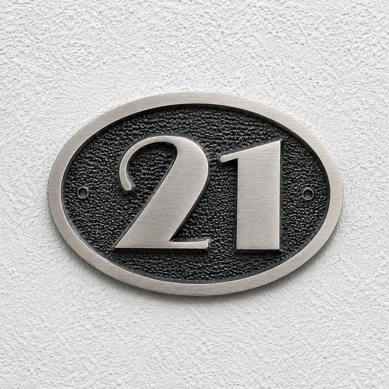 An oval house number plaque featuring the numbers '21' in brushed silver, mounted on a textured white stucco wall.