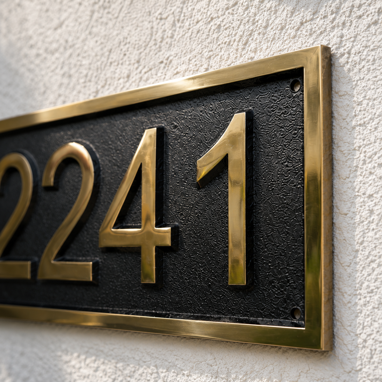 A close-up of a house number plaque showing the numbers 2241 in raised gold lettering on a textured black background, mounted on a white stucco wall.