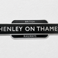 A black vintage-style station sign reading 'HENLEY ON THAMES' with 'BRITISH RAILWAYS' above and below, mounted against a light textured wall.