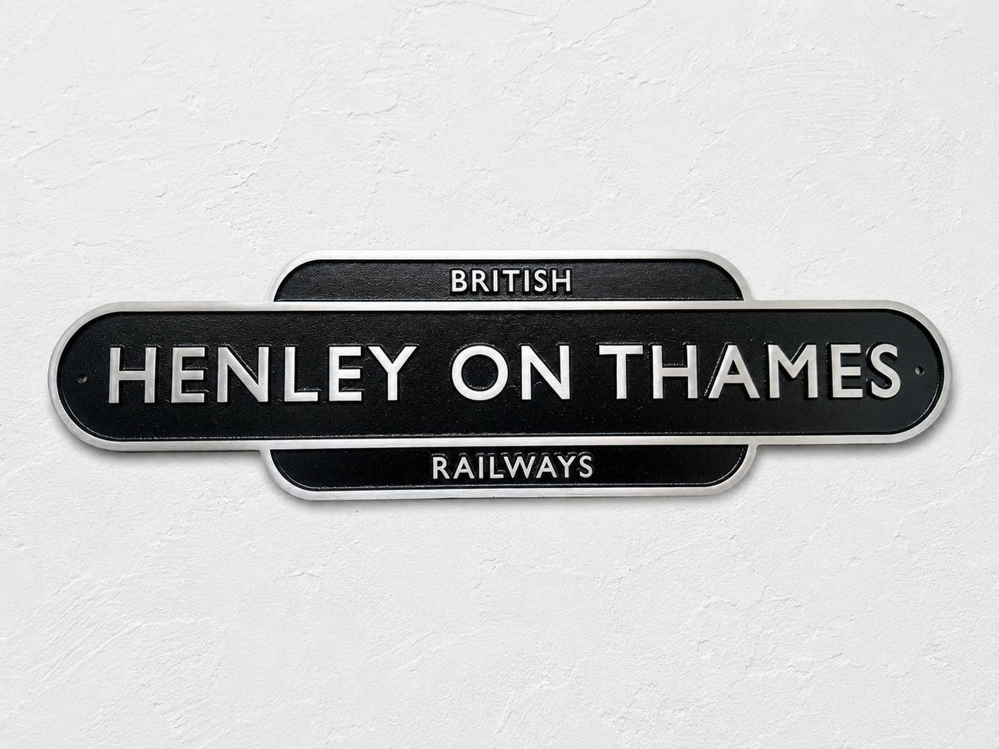 A black vintage-style station sign reading 'HENLEY ON THAMES' with 'BRITISH RAILWAYS' above and below, mounted against a light textured wall.