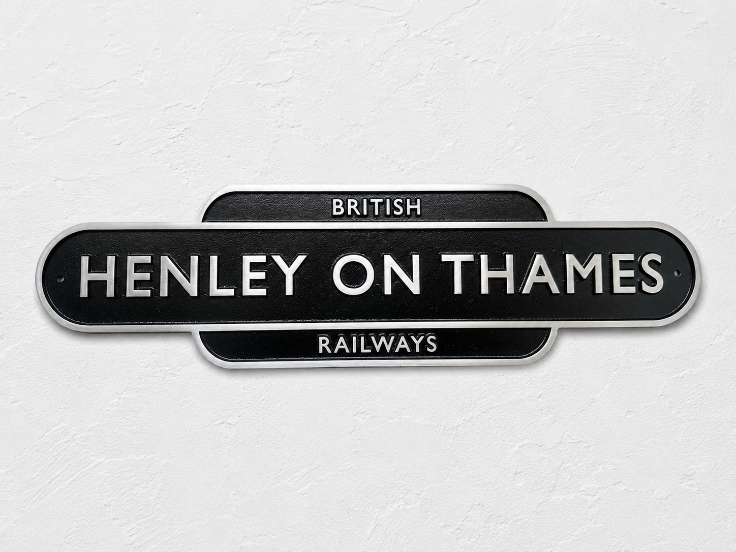 A black vintage-style station sign reading 'HENLEY ON THAMES' with 'BRITISH RAILWAYS' above and below, mounted against a light textured wall.