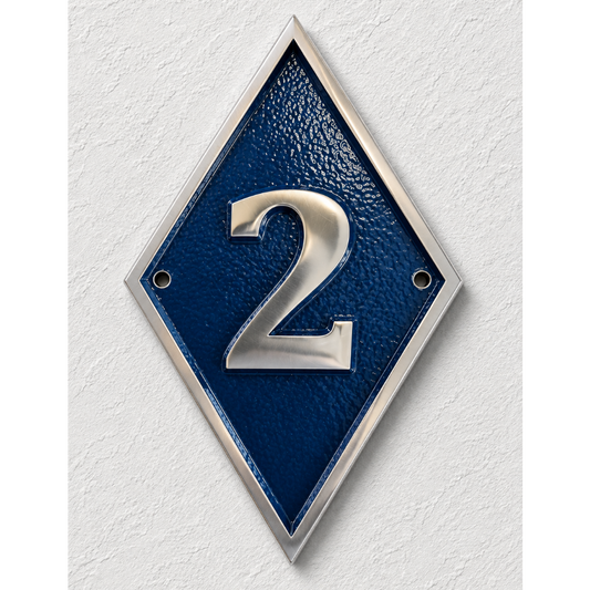 A diamond-shaped house number plaque with a textured dark blue center, silver metallic border, and a raised silver number 2, mounted on a white textured wall.