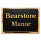 A rectangular black plaque with raised gold lettering reading 'Bearstone Manor' and a polished gold border, shown on a plain white background.