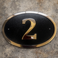 Cast bronze oval house number sign with polished raised numeral and black background

