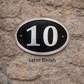 Cast aluminium oval hotel room number sign with raised numbers and black background mounted on wall