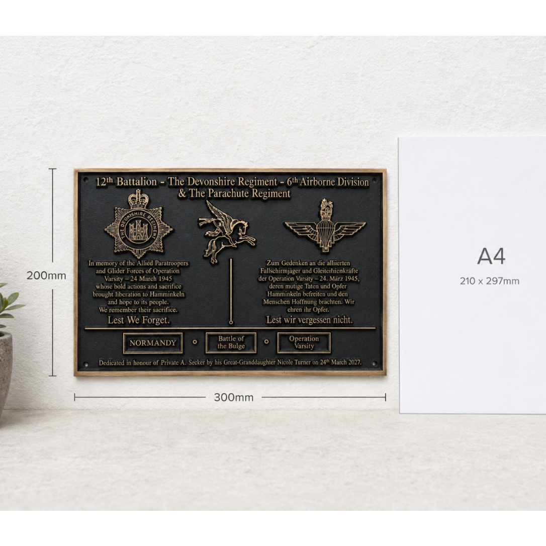 A rectangular black commemorative plaque with raised gold-toned text and military insignia, shown on a light wall beside a white A4 paper size reference card. Measurement labels on the left indicate 200mm height and 300mm width.