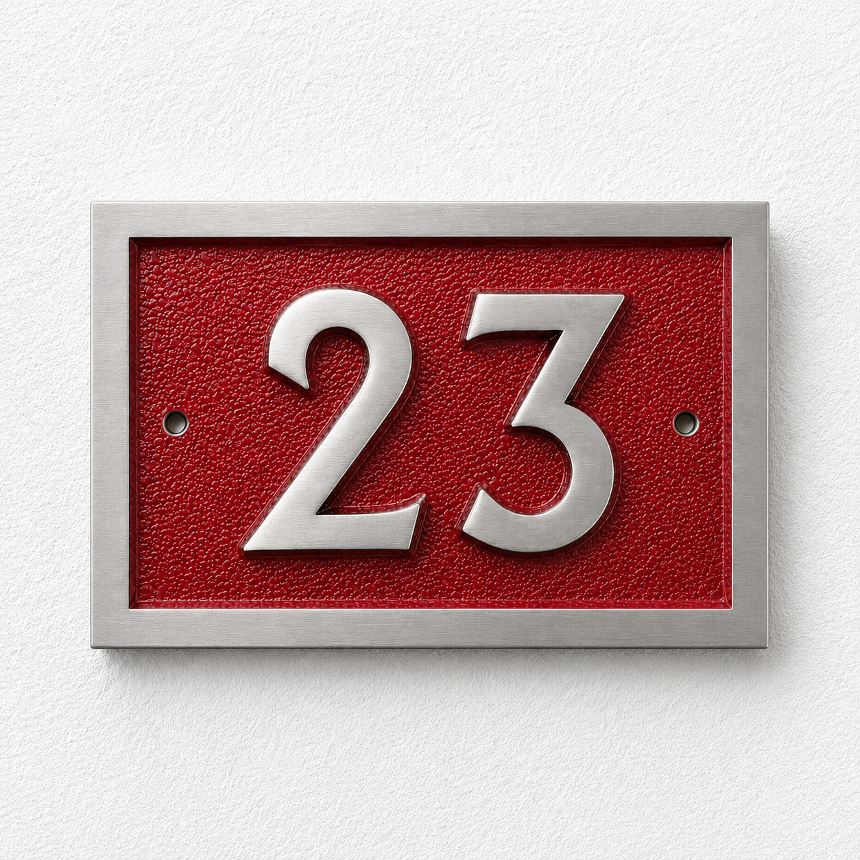 A modern house number plaque featuring the number 23 in raised silver-tone metal over a textured red background, mounted on a white textured wall.