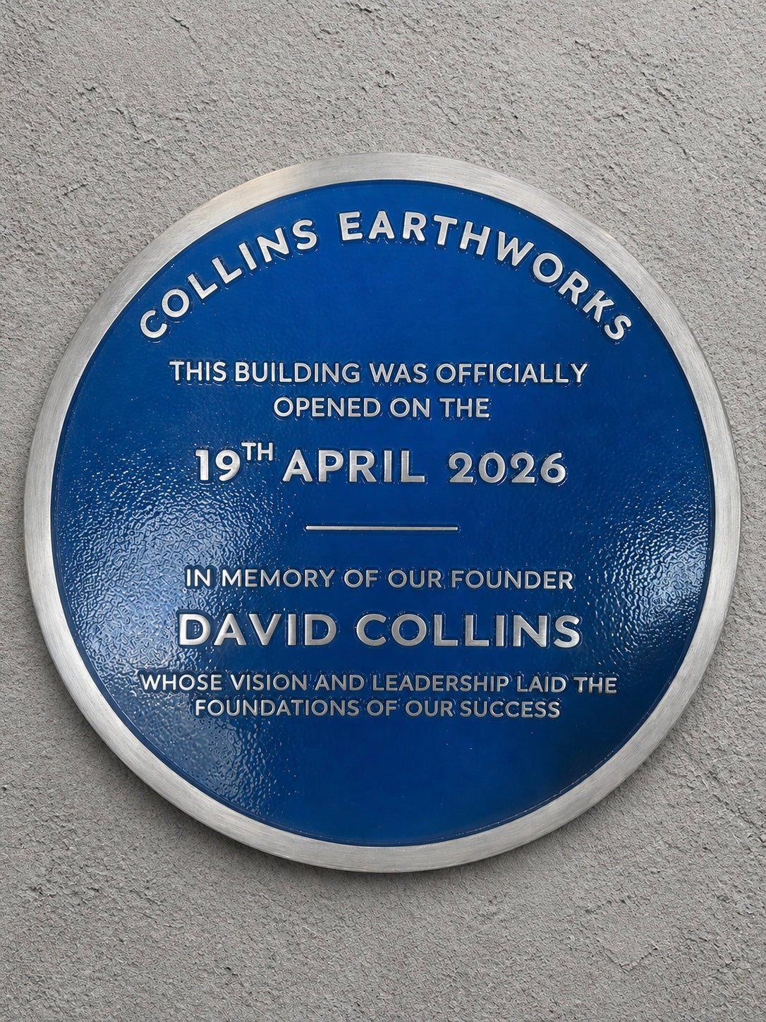 Modern blue heritage plaque with brushed silver border and raised lettering mounted on exterior wall