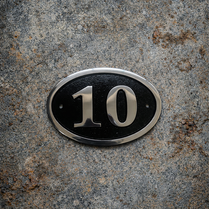 Cast aluminium oval hotel room number sign with raised numbers and black background mounted on wall