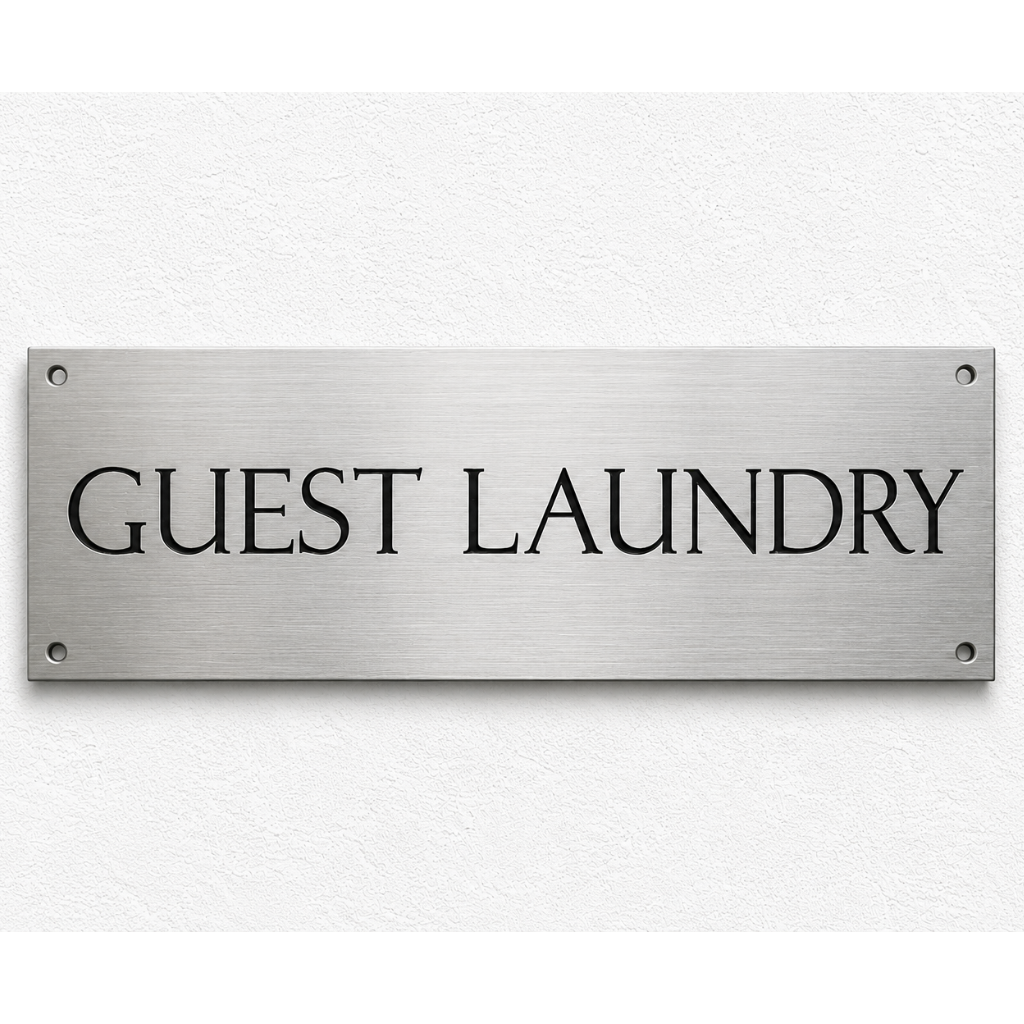 A rectangular brushed metal sign with the words 'GUEST LAUNDRY' in black serif lettering, mounted on a white textured wall.