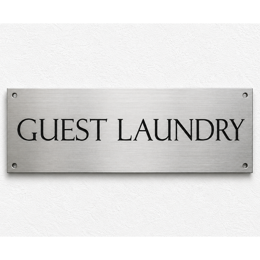 A rectangular brushed metal sign with the words 'GUEST LAUNDRY' in black serif lettering, mounted on a white textured wall.