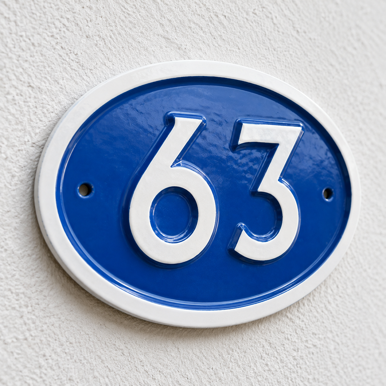 An oval blue and white house number plaque showing the number 63, mounted on a textured off-white wall.