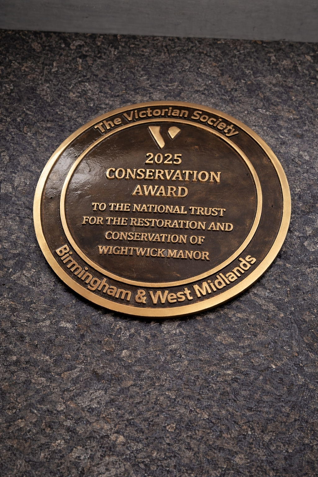 Cast bronze circular heritage plaque with raised lettering mounted on exterior wall