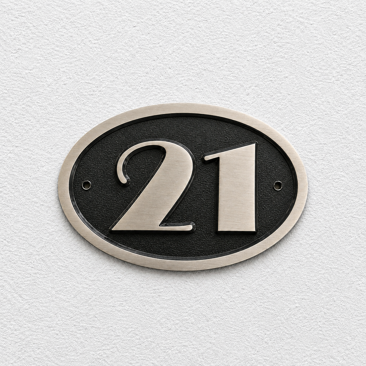 An oval house number plaque featuring the number 21 in brushed silver metal over a textured black center, mounted on a white textured wall.